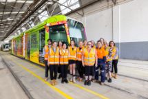 bunch of people in orange vests in front of a tram 