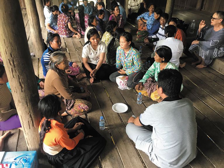 Three groups of people in Cambodia sitting in circles on a wooden floor in discussion
