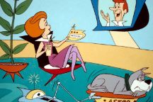 Jane Jetson talking to George Jetson on a TV screen, with a robot bothering the dog that is trying to sleep 