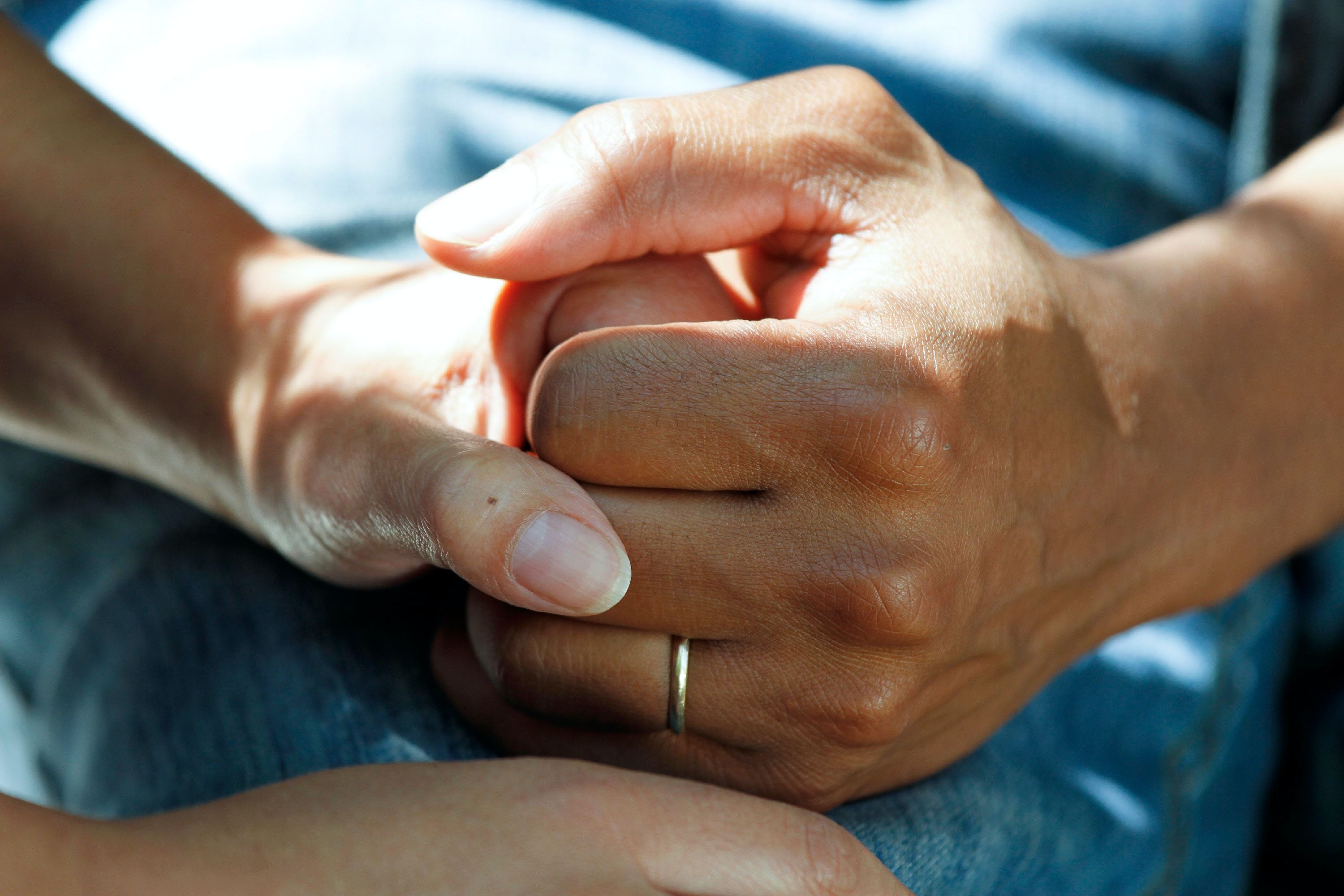 A hand with a wedding ring on its holds the hand of another person in a supportive and comforting gesture