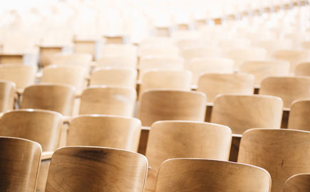 A view of an empty light filled lecture theatre with wooden chairs.