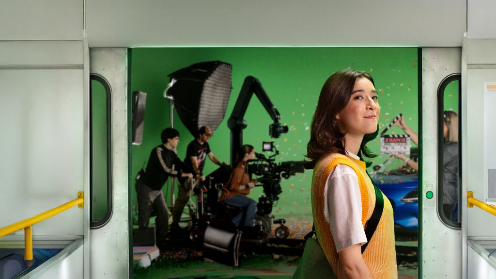 Young woman standing on a train as doors open to reveal a film set behind her.