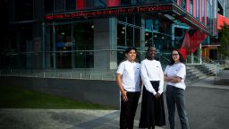 Three students wearing Swinburne branded clothing standing together on campus - cropped