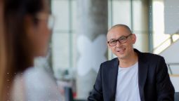 Image of bald man with glasses consulting, with a person out of focus in the background.