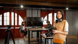 Woman holding a camera with headphones around her neck in a media studio.