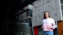 Young female woman stands in front of concrete logo Swinburne University in front of campus building.