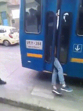 A blue bus drives away with a mans legs dangling out the door