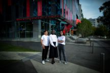 Three students wearing Swinburne branded clothing standing together on campus