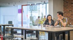 2 Students sitting at a desk, smiling and studying in the FS building.