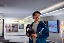 Person holding a virtual reality headset inside a modern anatomy lab, with anatomical models and digital medical displays in the background.