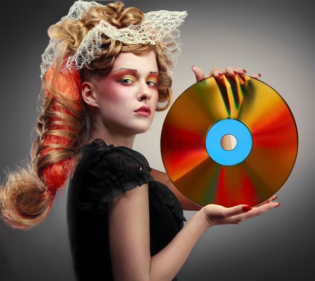 Woman with exaggerated makeup and lace in her hair holding up a laser disc