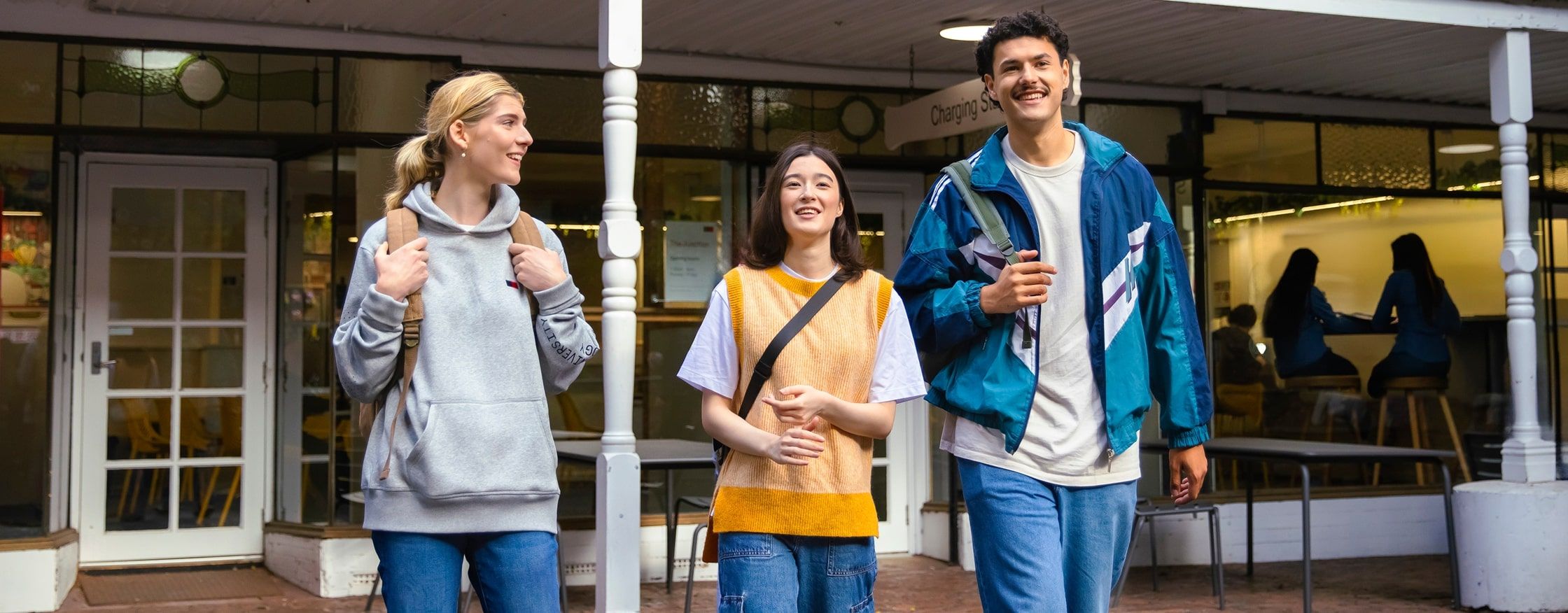 Three students walking and chatting outside a campus building, with a timeline graphic below showing steps from “Ready for Change” to “Unlock Your Ambitions.”