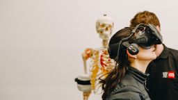 Young person using a virtual reality headset device to study anatomy, with a skeleton in the background.