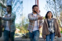 Two Swinburne students walk and talk together outside on Hawthorn campus, reflected in a glass wall behind them.