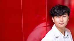 International student Josh from China standing in front of red wall
