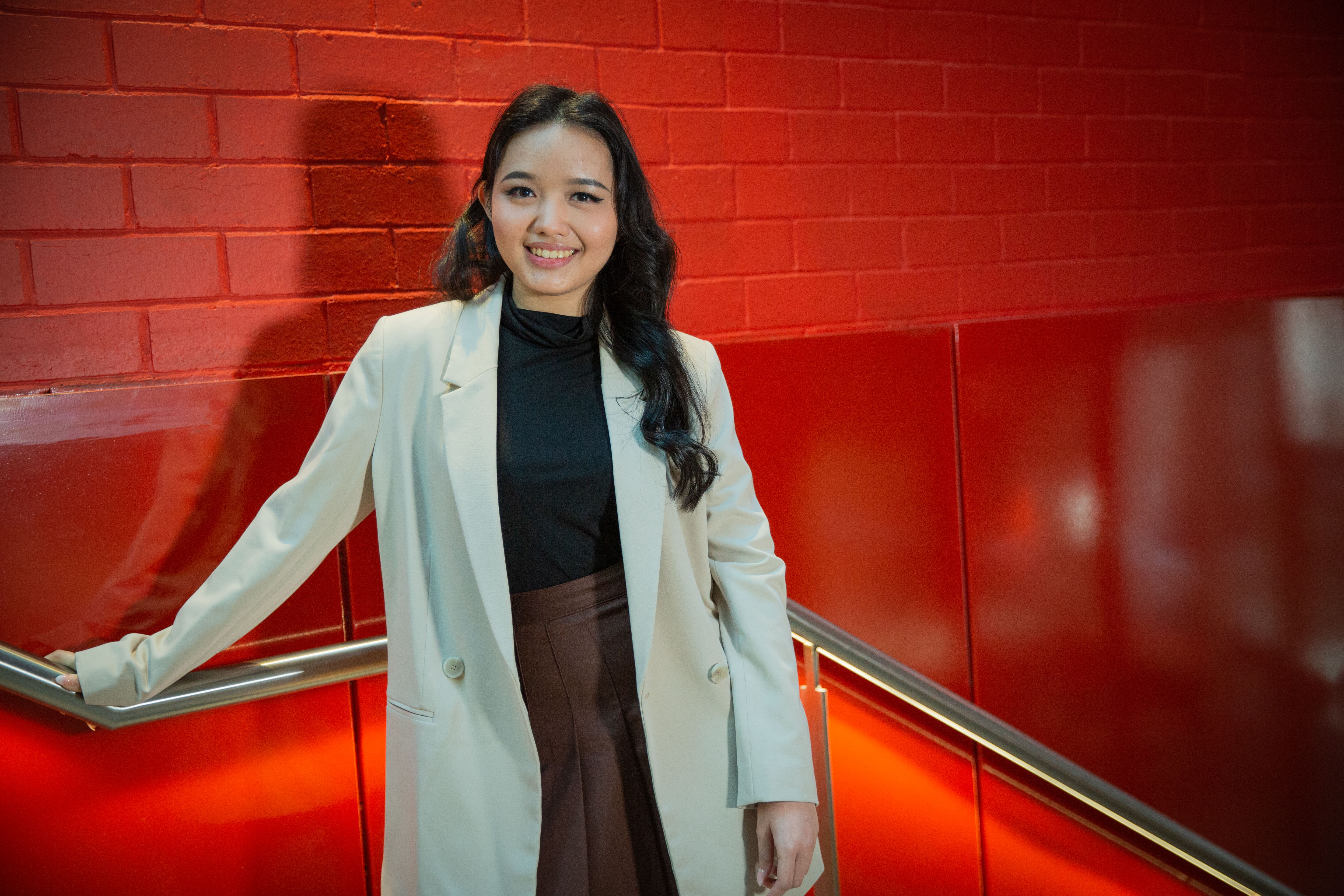 A female international student smiling and facing the camera in front of a red background.