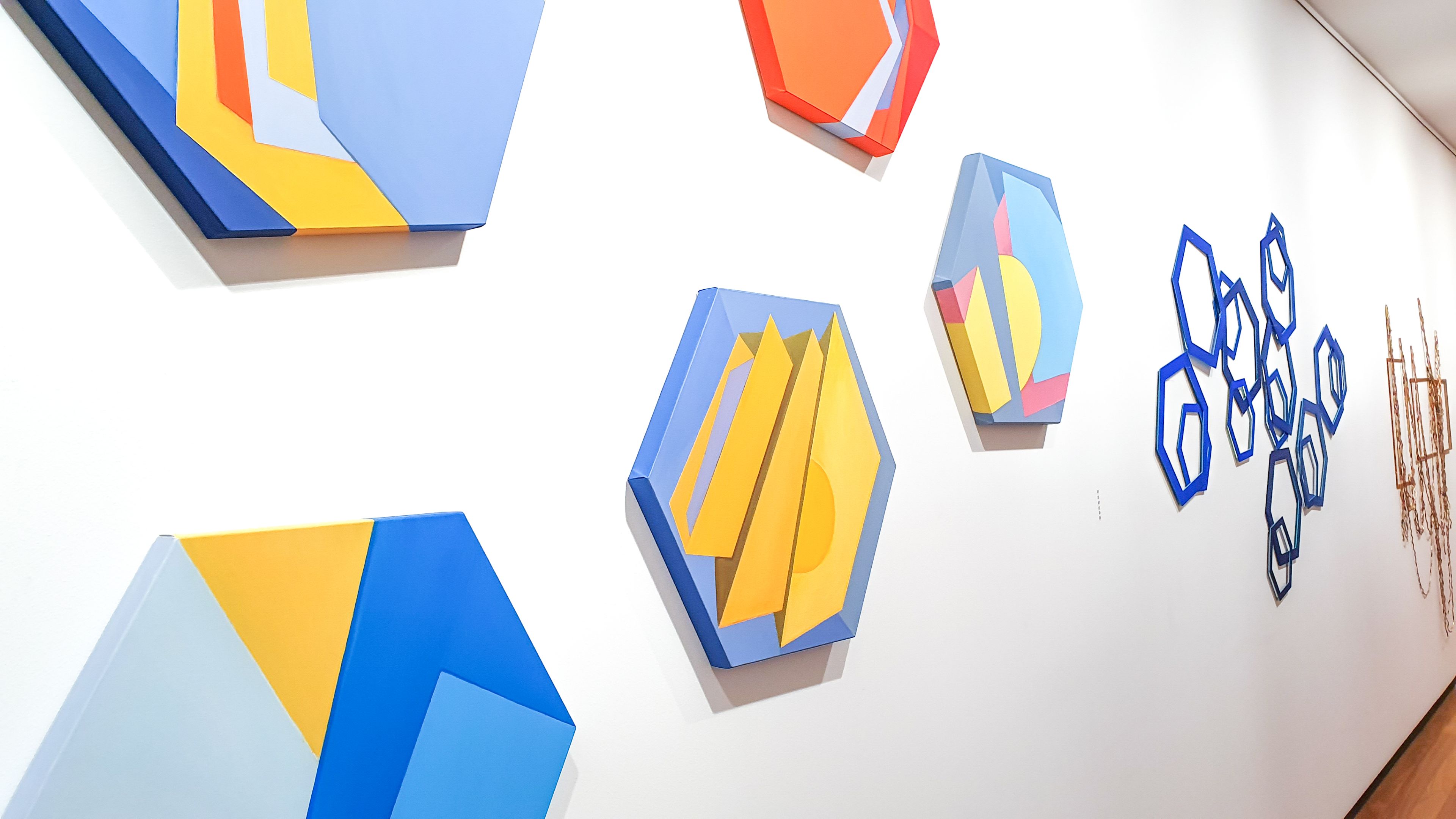 A series of brightly coloured geometric artworks hang on a white wall in the Boroondara Town Hall Gallery