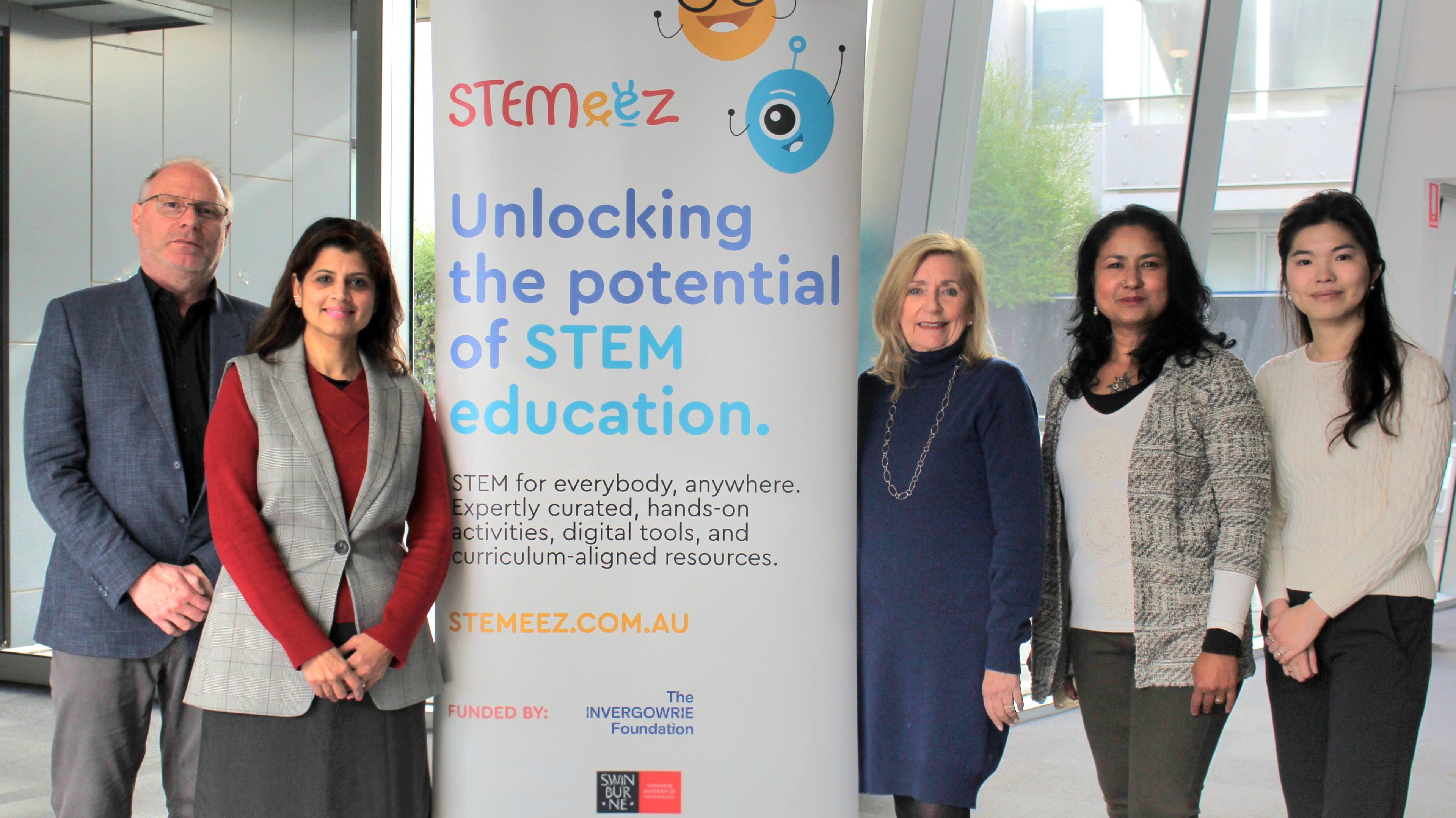 Team standing in front of a banner for 'STEMeez: Unlocking the potential of STEM education'.