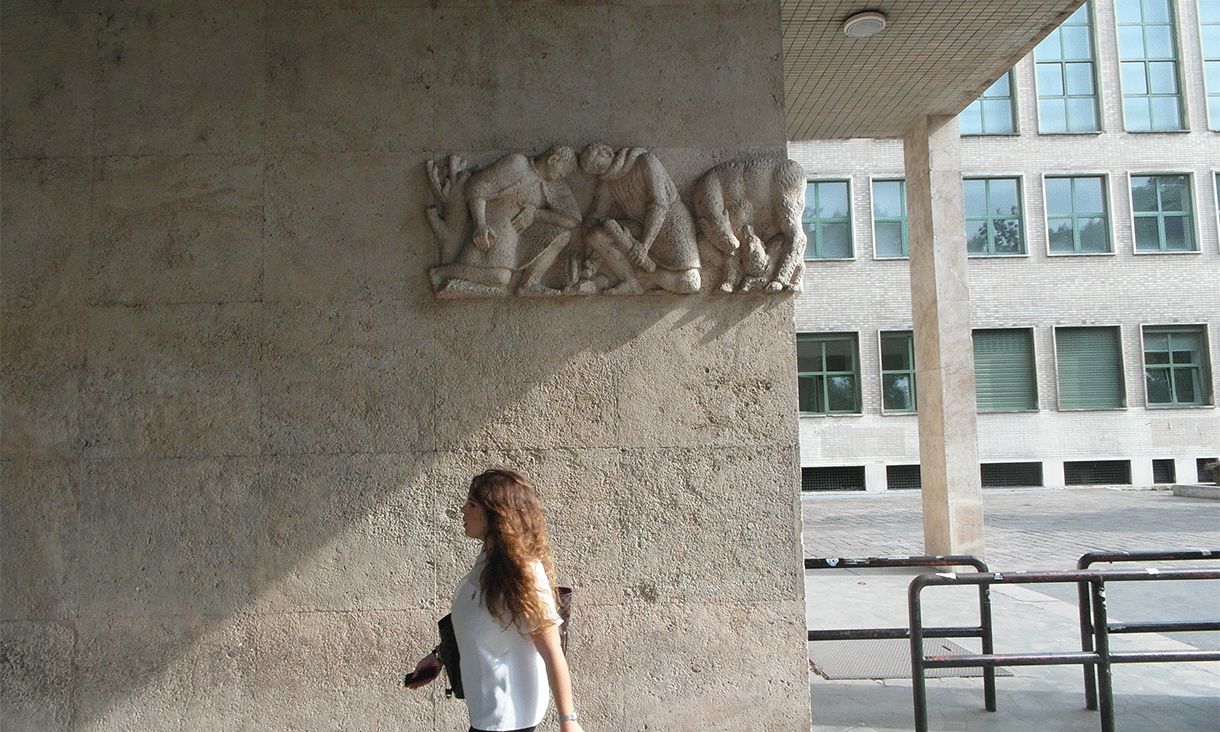 Woman in white top walking by a building an Bocconi University, Milan