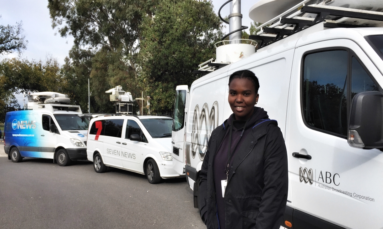 Ivy standing next to the white ABC van on the street, wearing dark clothing and smiling at the camera