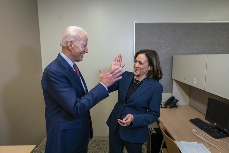 Joe Biden in a blue suit giving Kamala Harris, also in a blue suit, a high-five in an office space