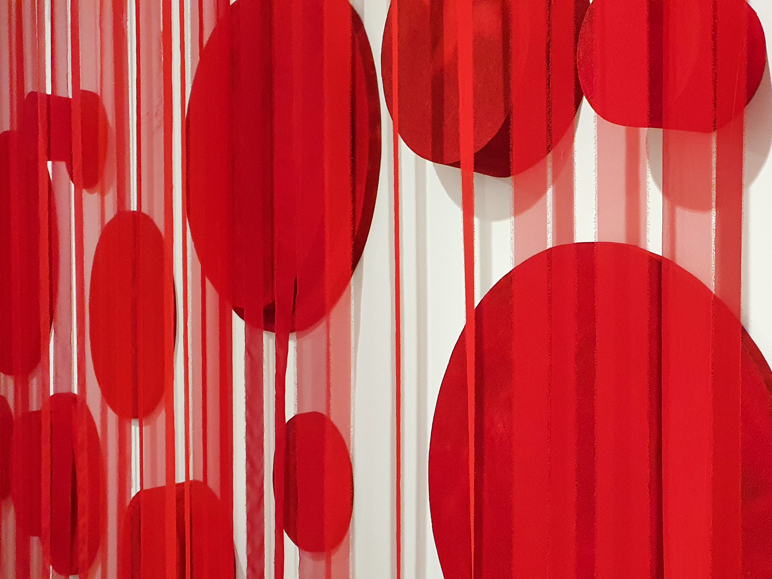 A series of red foam circles of different sizes are spread across a white wall and covered by a curtain of cloth streamers