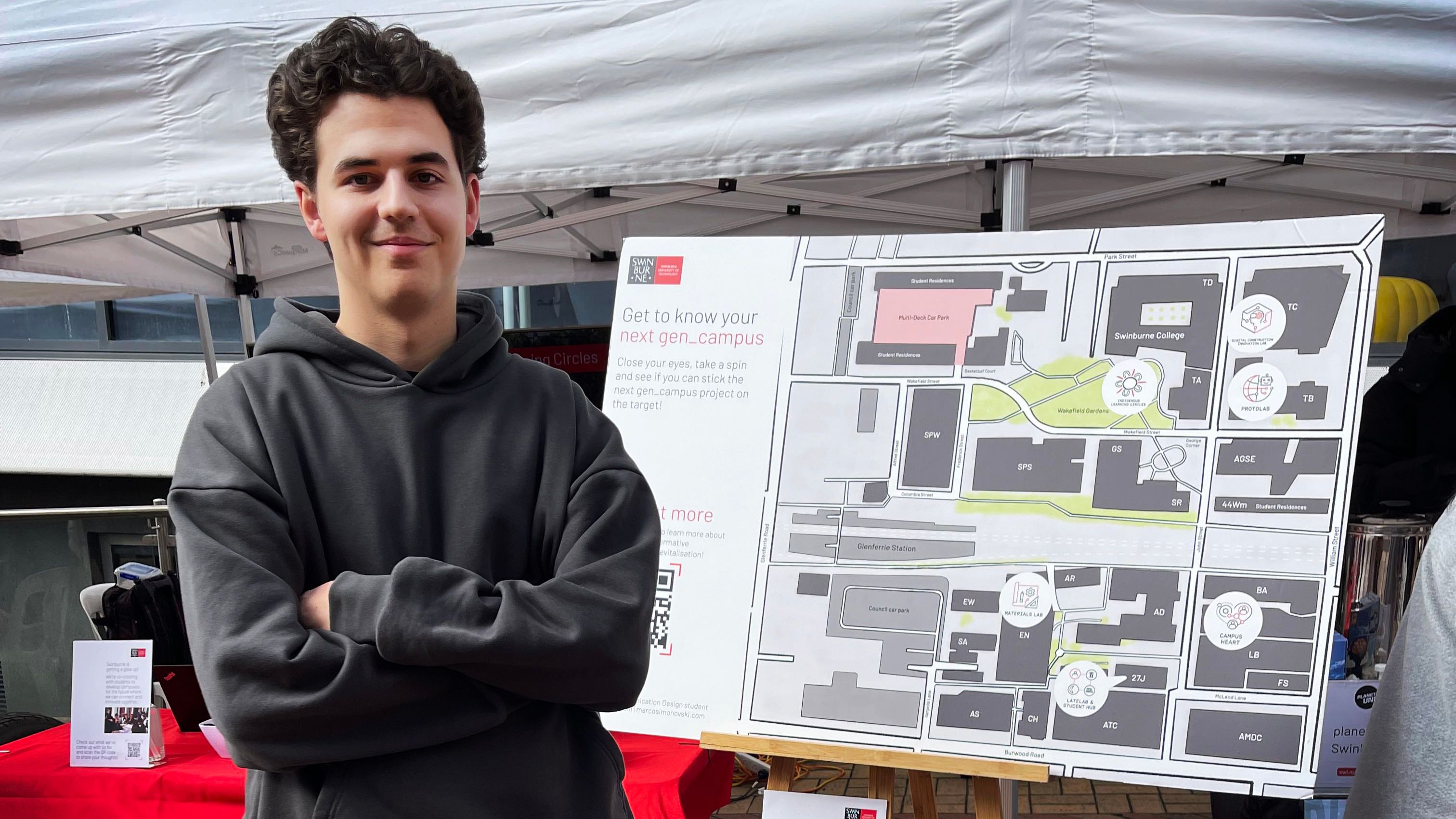 A student with his arms crossed smiles at the camera in front of a map of Swinburne's Hawthorn campus
