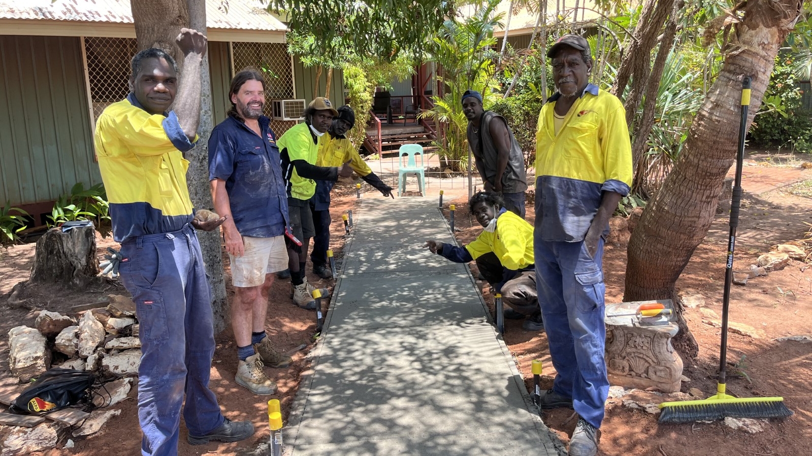 Swinburne’s Head of Croydon Bricklaying Department Matt O’Brieni is picture standing by a footpath with members of one his classes. They are all lined up on either side of the path. They wear work gear and various tools are visible in the background 