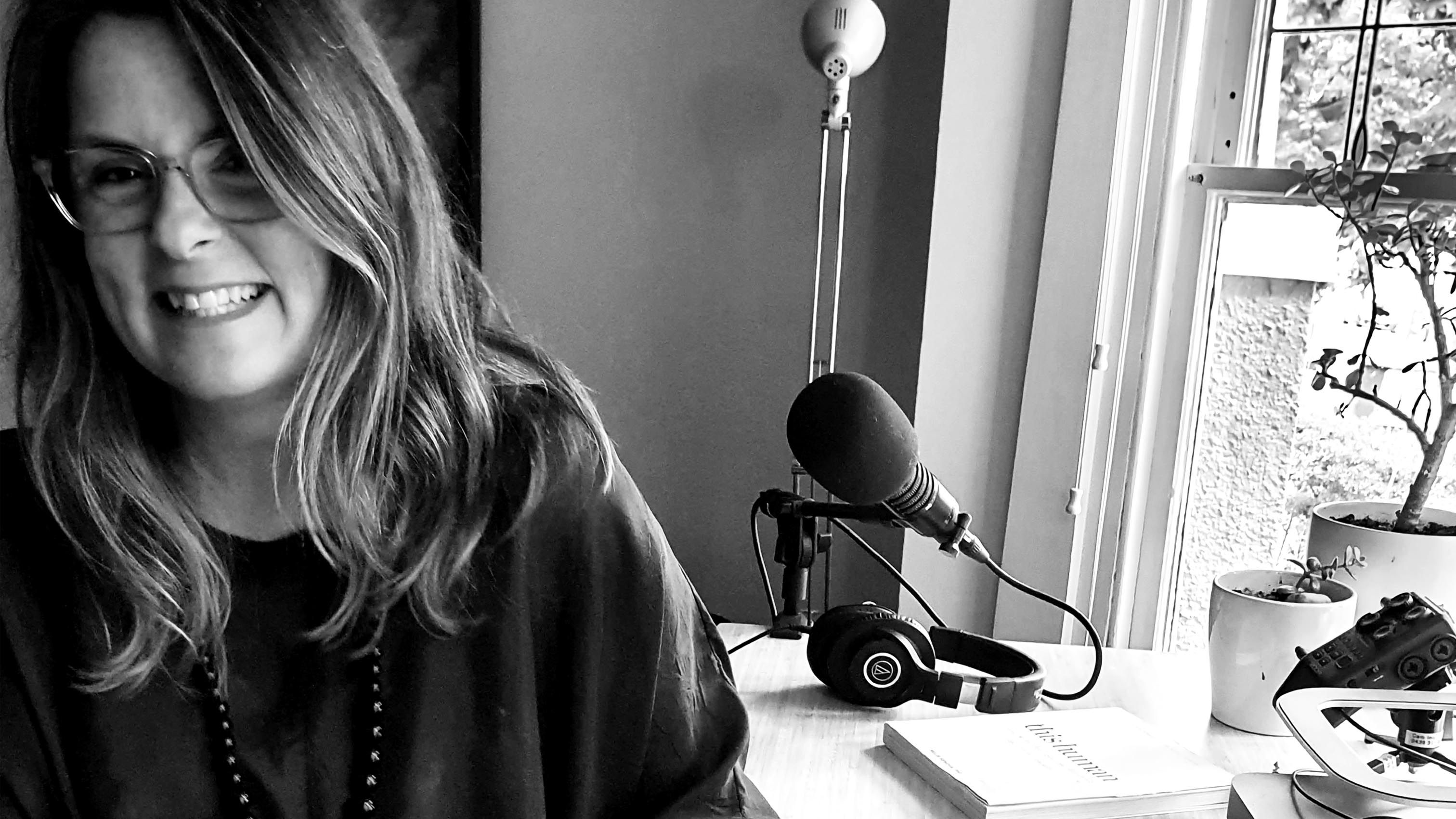 Swinburne alum Melis Senova sitting at a desk with a microphone and headphones and a copy of her book This Human on the desk