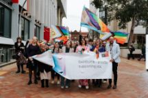Group of people standing in front of a banner that says "Swinburne proudly supporting you" waving pride flags