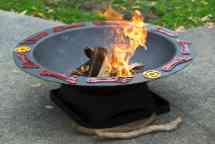 A round, black fire pit with decorative red feet and yellow circle symbols around the edge and a fire burning inside.