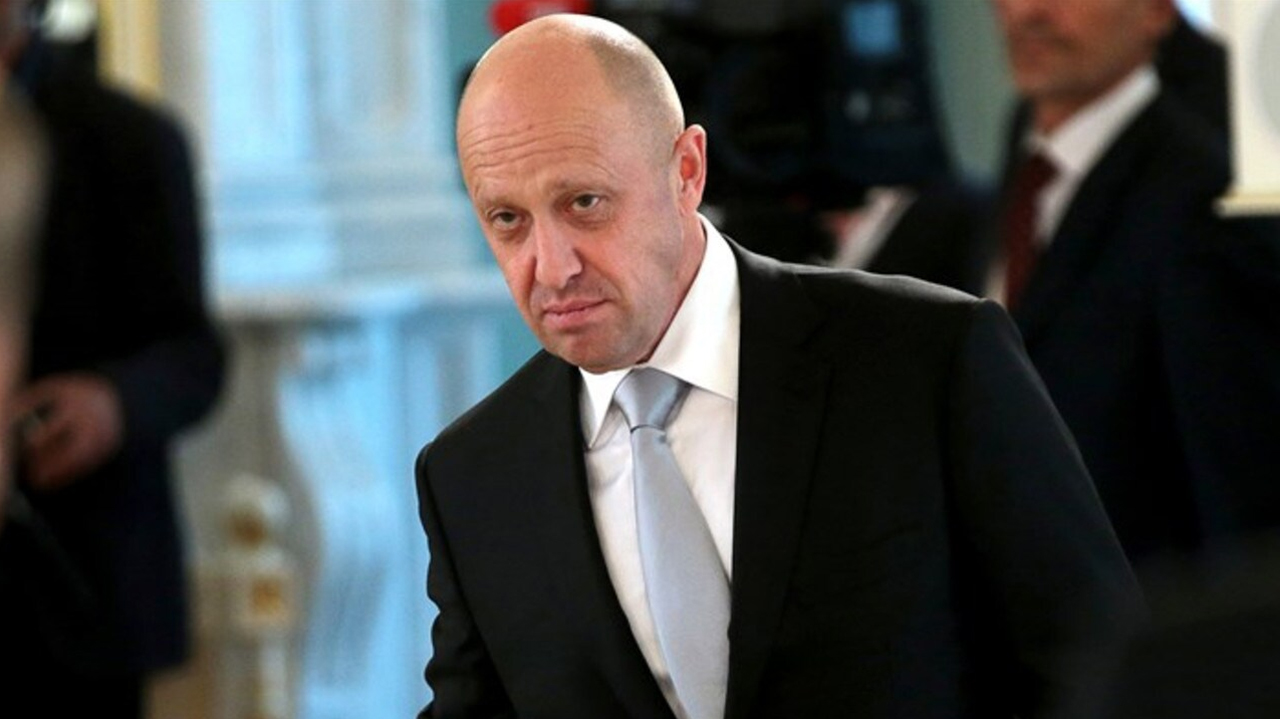Russian oligarch Yevgeny Prigozhin wearing a black suit, white shirt and grey tie with others in black suits behind