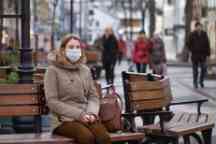 Woman in brown clothing sitting on a bench seat wearing a facemask