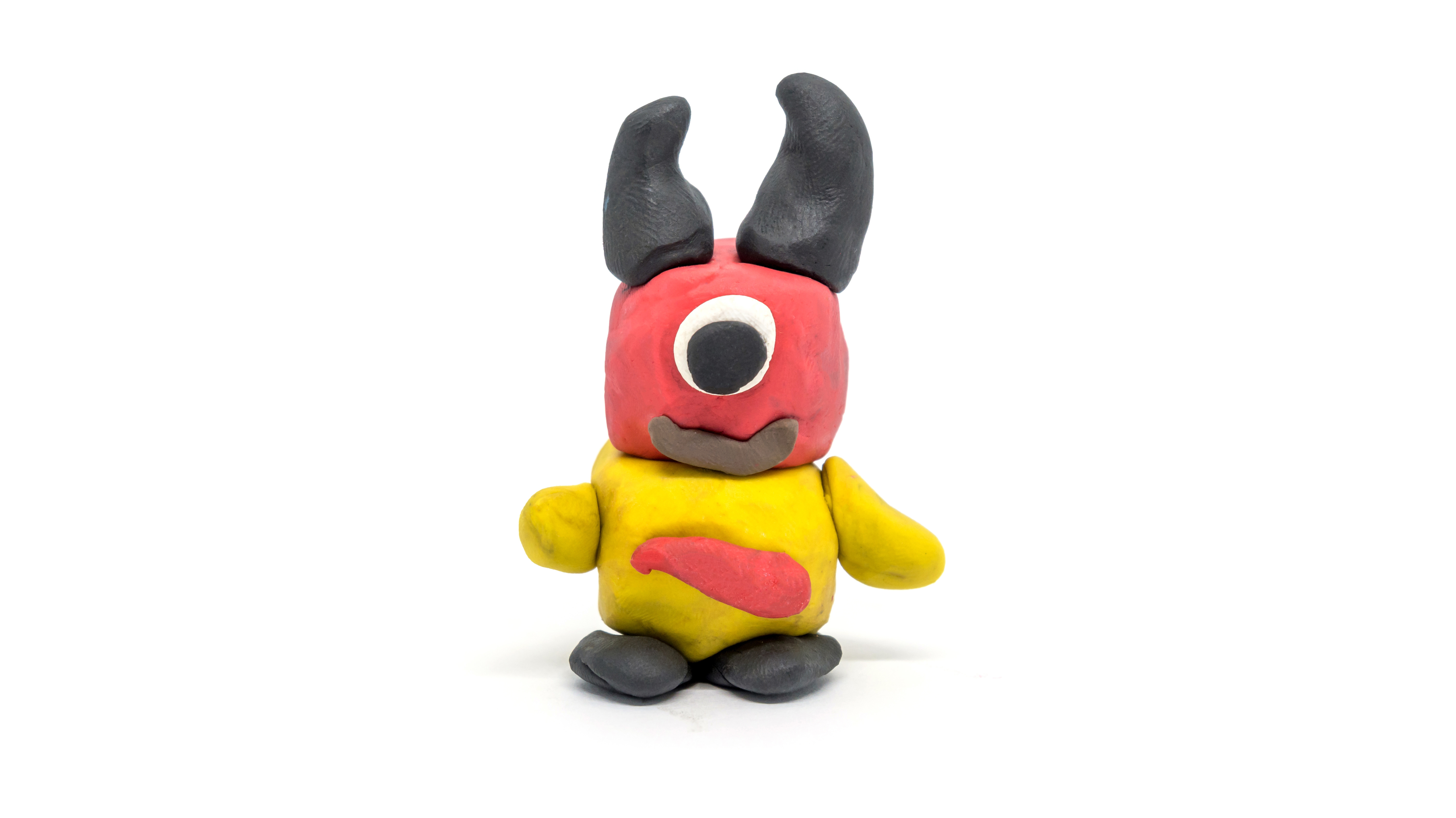 One-eyed, red, black and yellow plasticine monster on white background