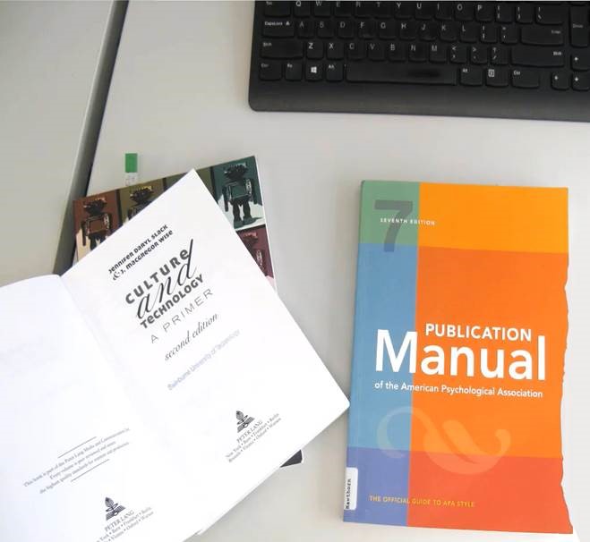 Assorted text books on a desk and a black computer keyboard obscured in the top right hand corner.