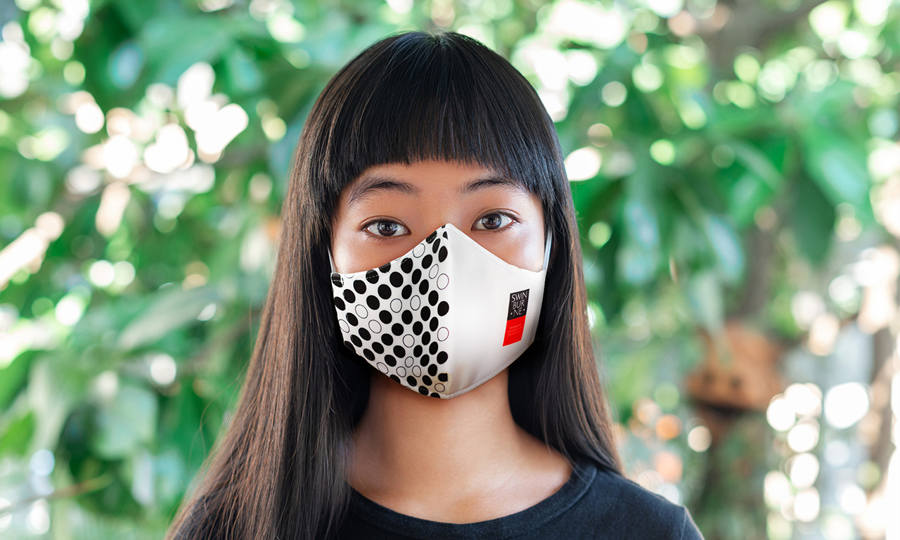Woman wearing a face mask branded with Swinburne logo and facade of Advanced Technologies Building