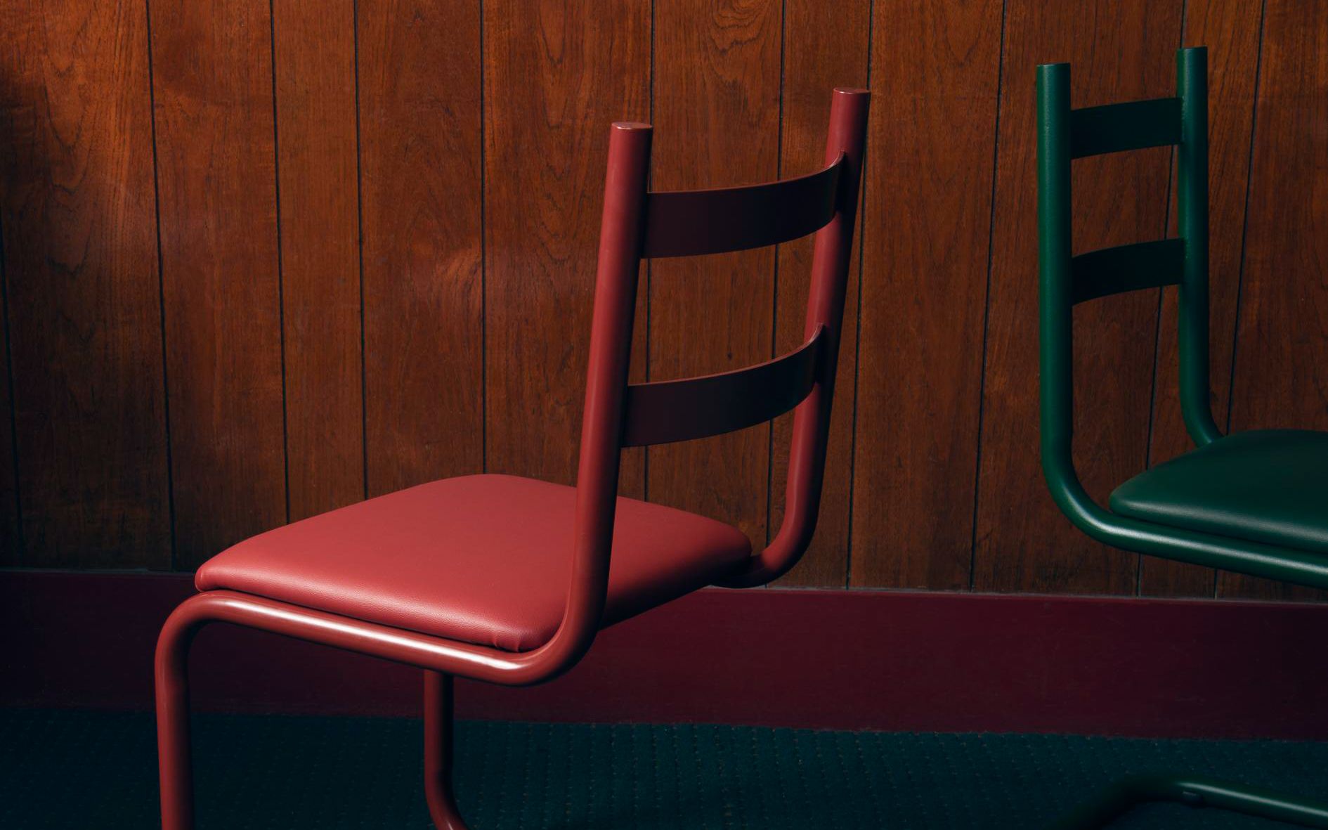 Red and green steel chairs against dark wood panel background