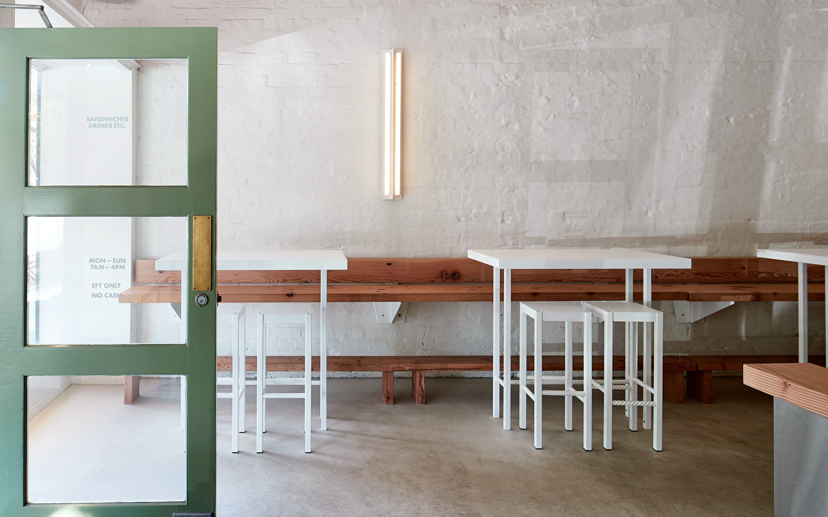 A series of white steel tables and stools in an airy, rustic space with white painted walls and a open door
