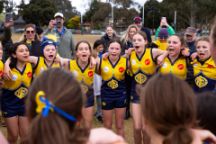 Young girls from the Yarra Junior Football League stand arm in arm celebrating a win. They are in the middle of singing their club song.