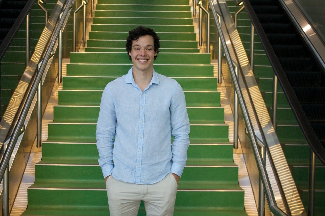 Angus Delaney at the bottom of green stairs wearing a blue shirt, smiling with his hands in his pocket.
