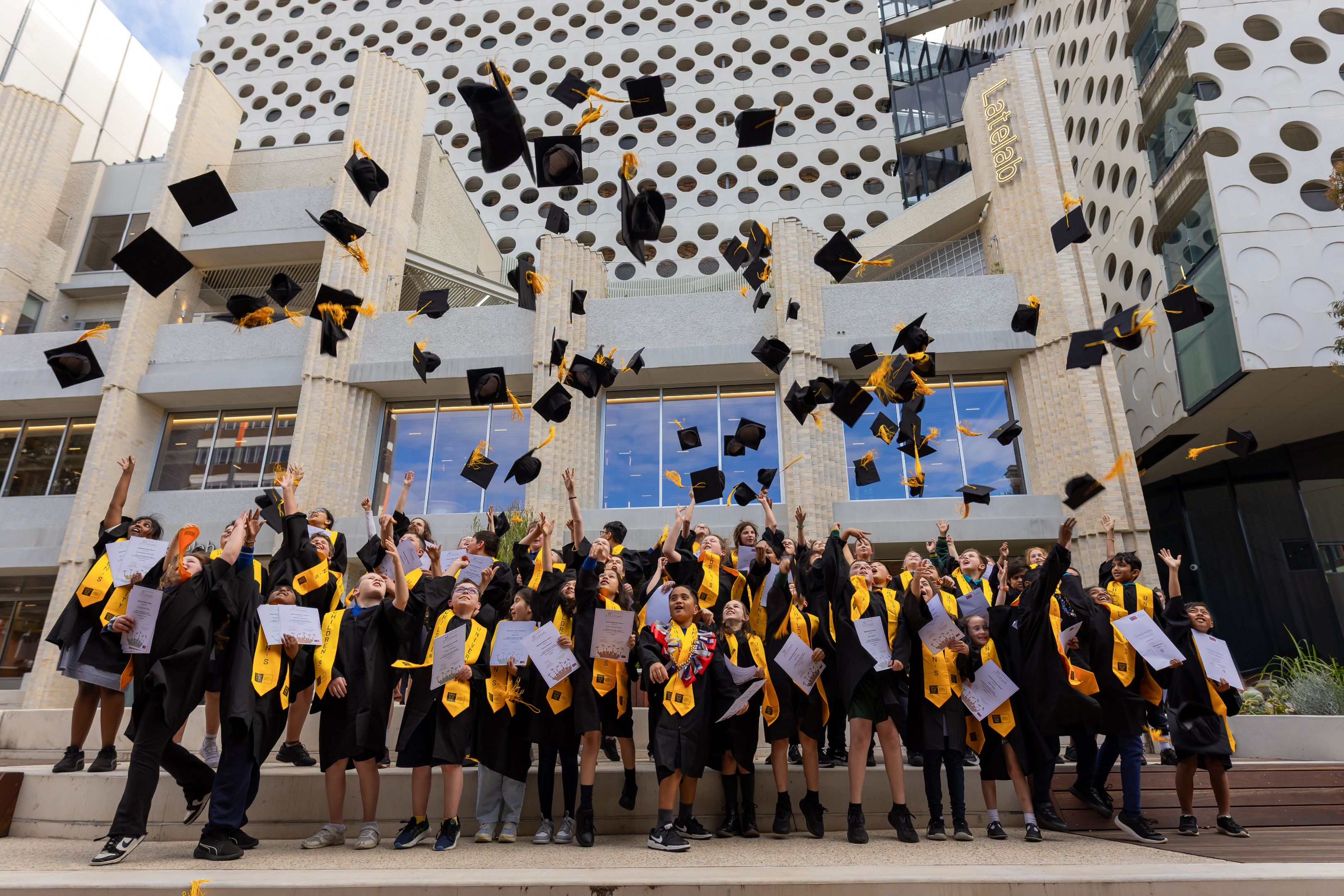 Children dressed in university graduation attire throw their hats in the air at Swinburne's Hawthorn campus.