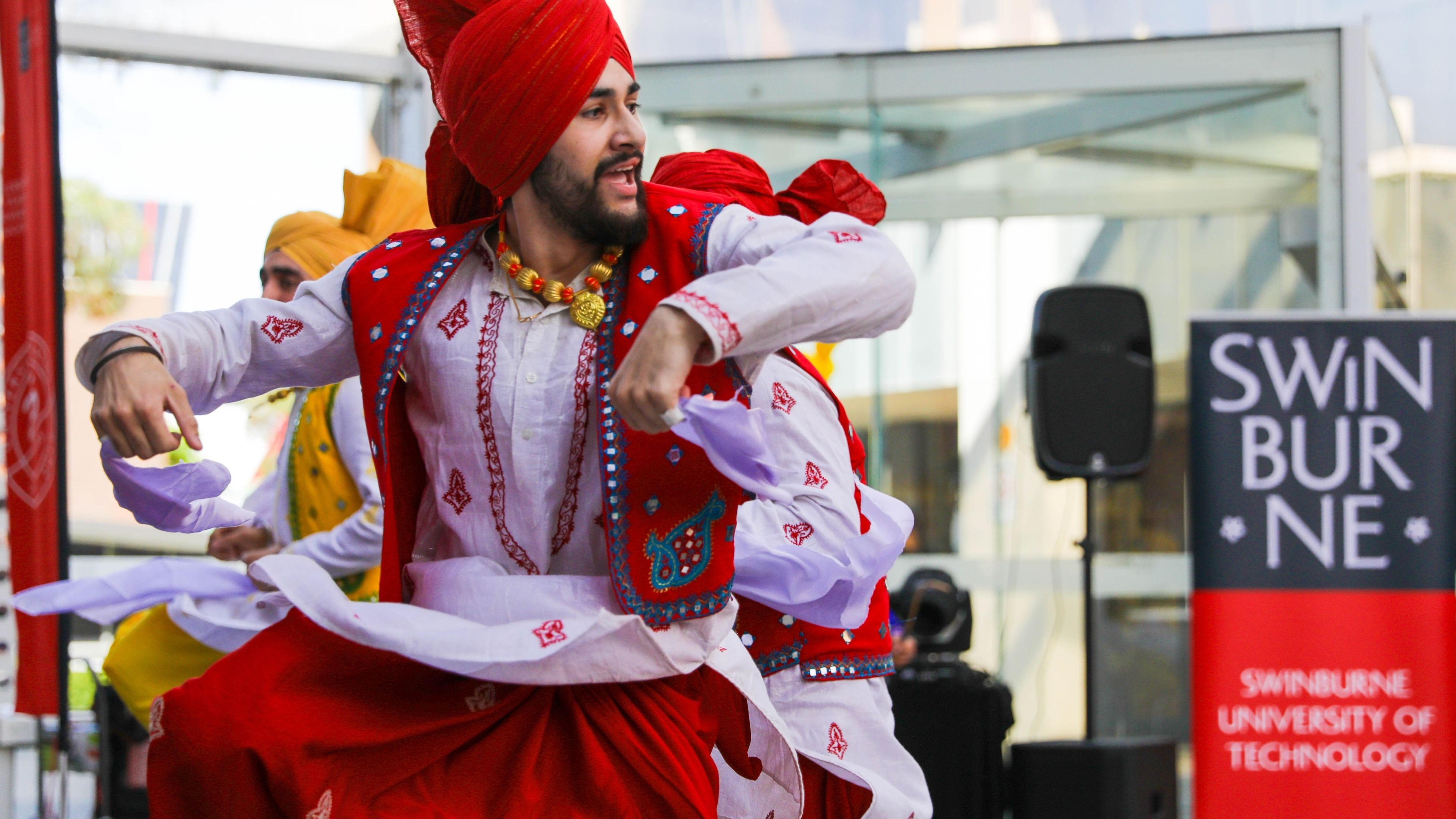Man wearing bright red traditional Diawli attire dances upon a Swinburne stage