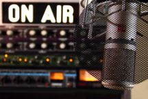 Microphone on the right in front of a sound engineering console with the words On Air illuminated