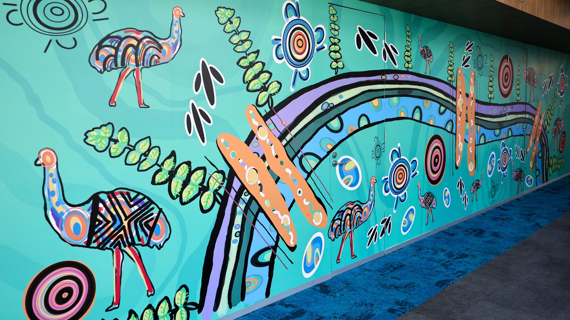 Indigenous artwork by Mandi Barton, featuring emus, bright colours and flowing lines along a wall. 