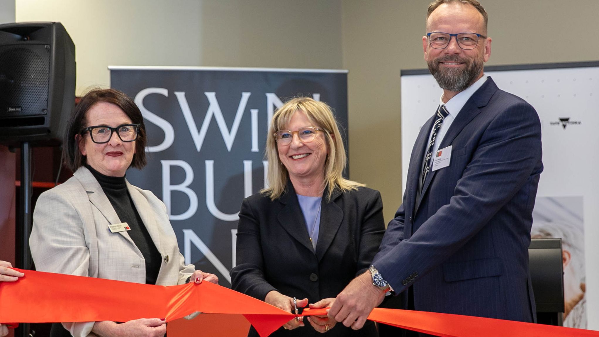 Three people cutting a ribbon at an official launch.