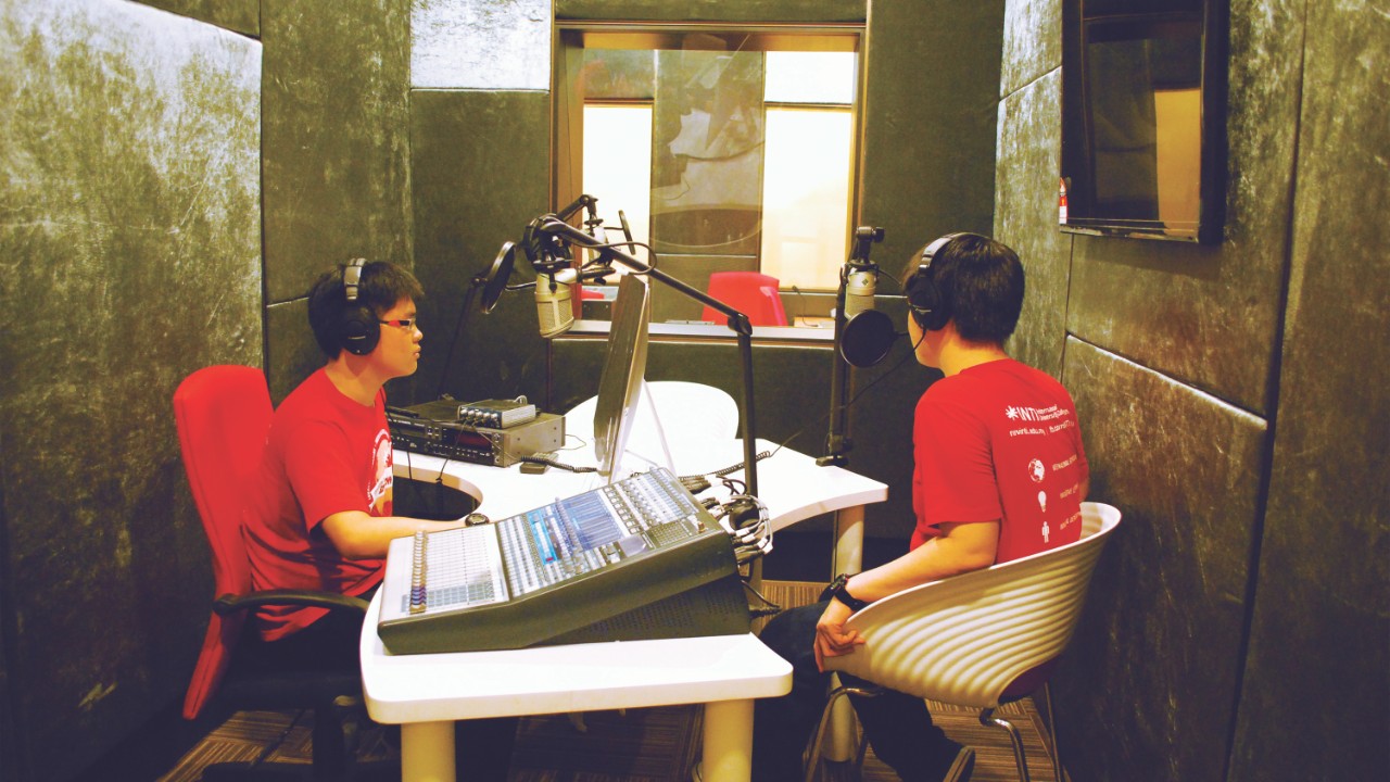 Two students in a small broadcasting studio with headphones and microphones.