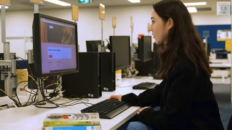 A woman wearing a black sweater viewing the Swinburne website at a desk with multiple desktop computers.