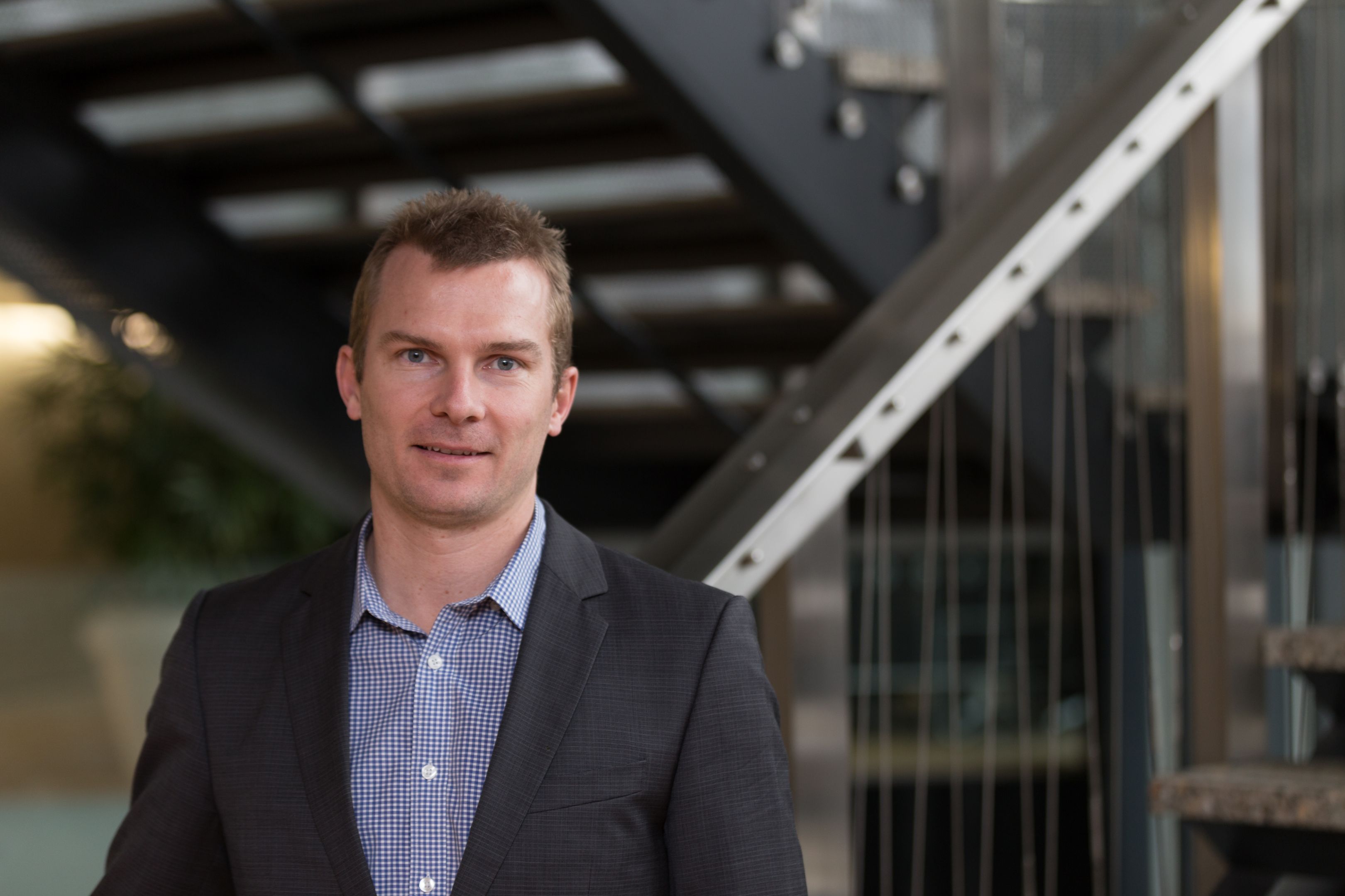 Photograph of Jarrod Mitchell from Melbourne water. Jarrod stands in front of a staircase and is wearing a suit jacket and shirt.