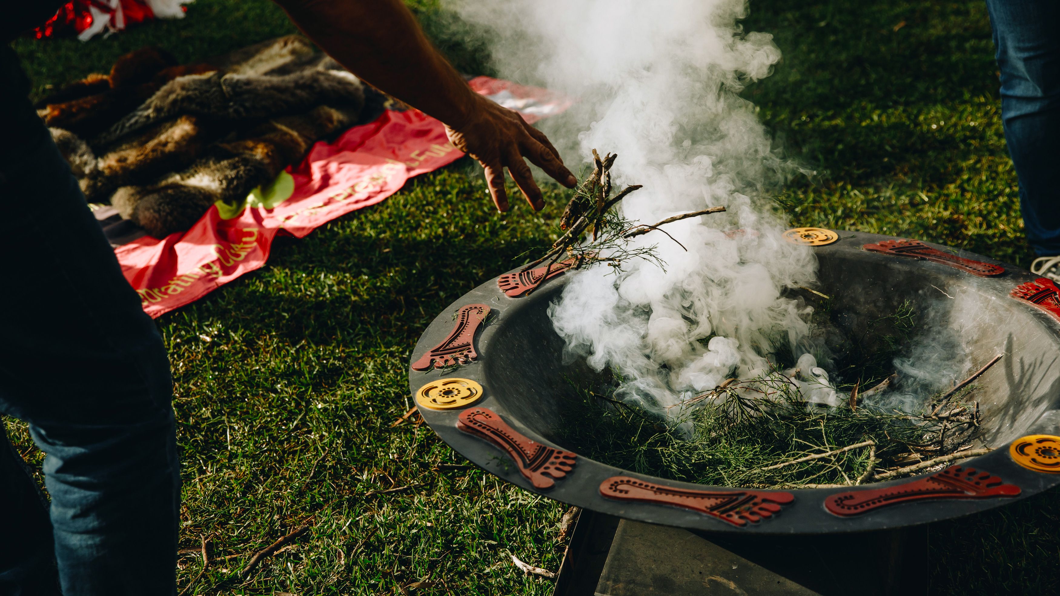 An Indigenous smoking ceremony wih leaves and sticks in a decorated firepit.