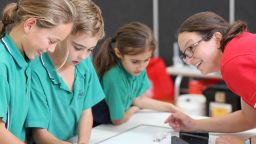 Three primary school students working at a table with a PrimeSCI! educator watching them.